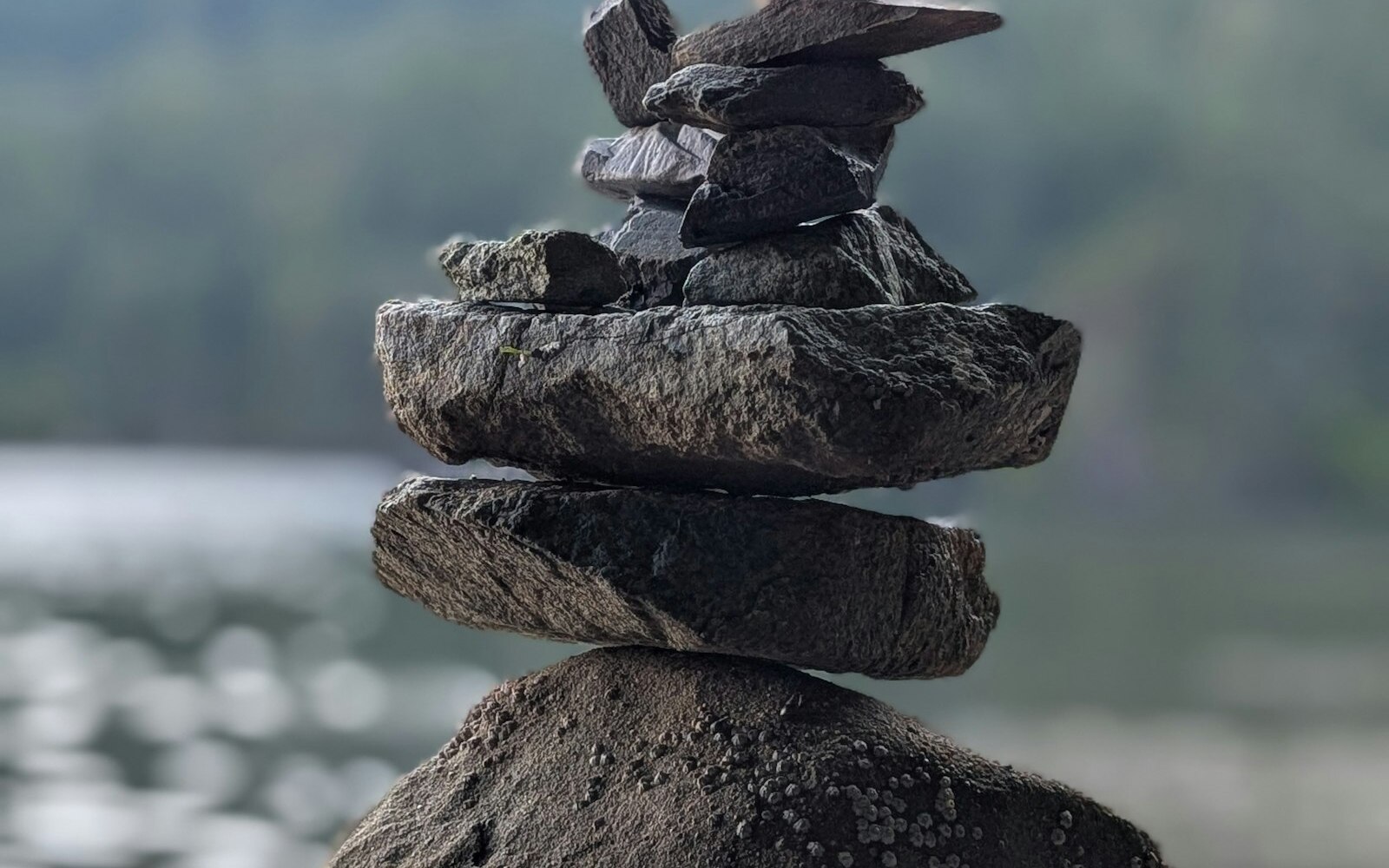 Stack of balanced stones by a calm lake with mountains, symbolizing balance and contemplation